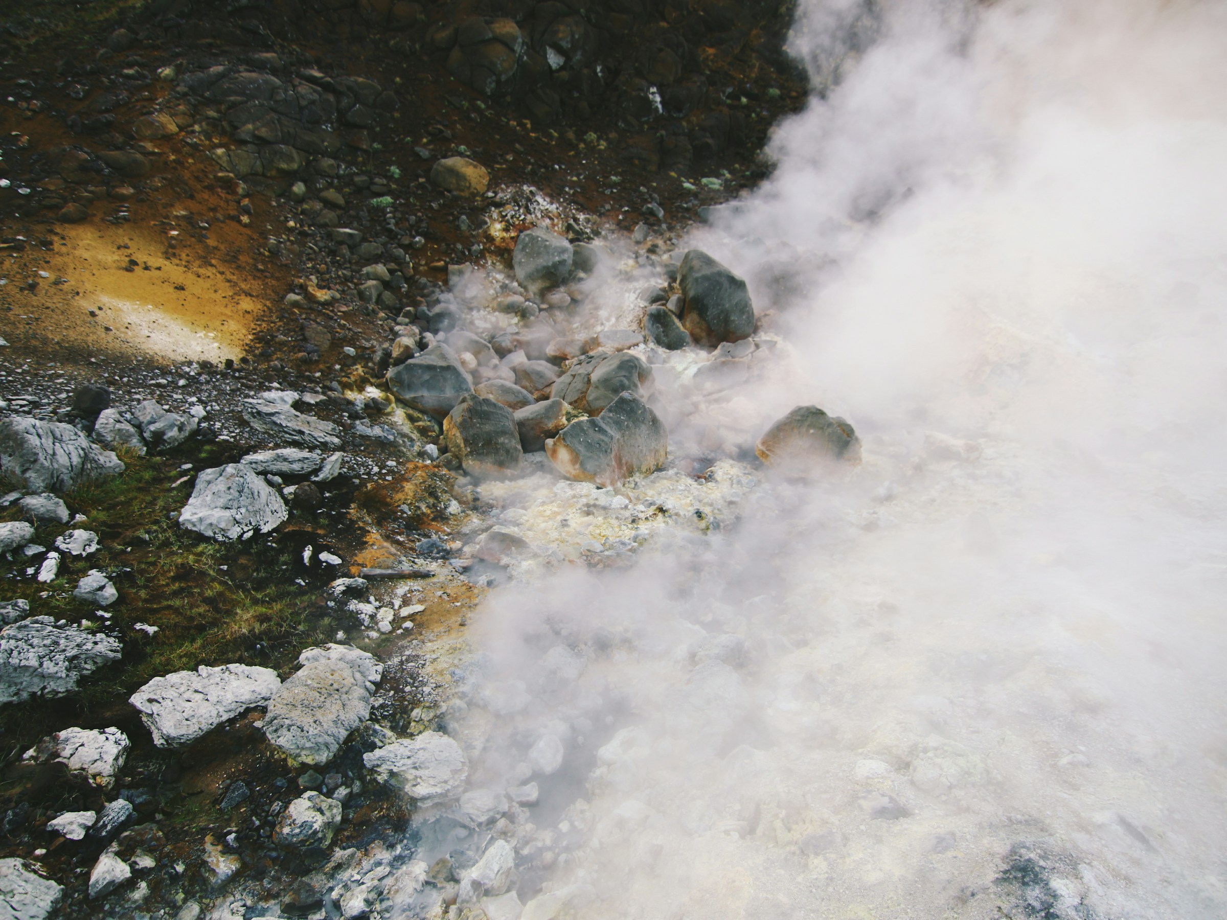 A natural hot spring pool held in dark rock, steam lifting off the surface
